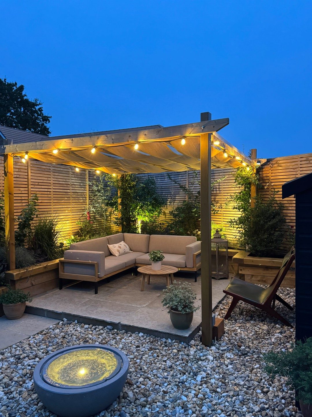 Garden pergola with festoon lights and uplit planting at dusk